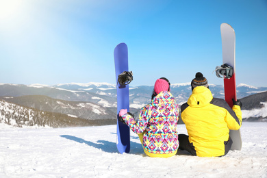 Photo of Young couple with snowboards on hill, back view. Winter vacation