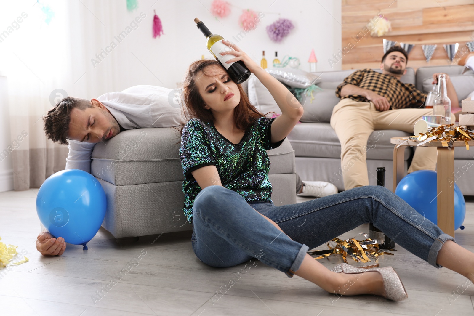 Photo of Young woman suffering from hangover and her friend sleeping in messy room after party