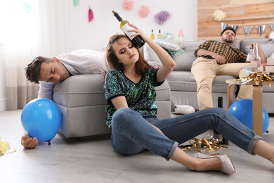 Young woman suffering from hangover and her friend sleeping in messy room after party