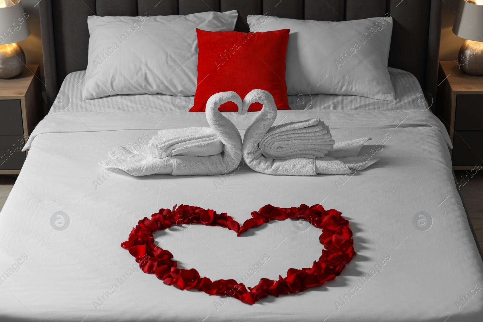 Photo of Honeymoon. Swans made with towels and heart of beautiful rose petals on bed in room