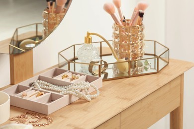 Jewelry box with many different accessories, perfume and makeup brushes on wooden table