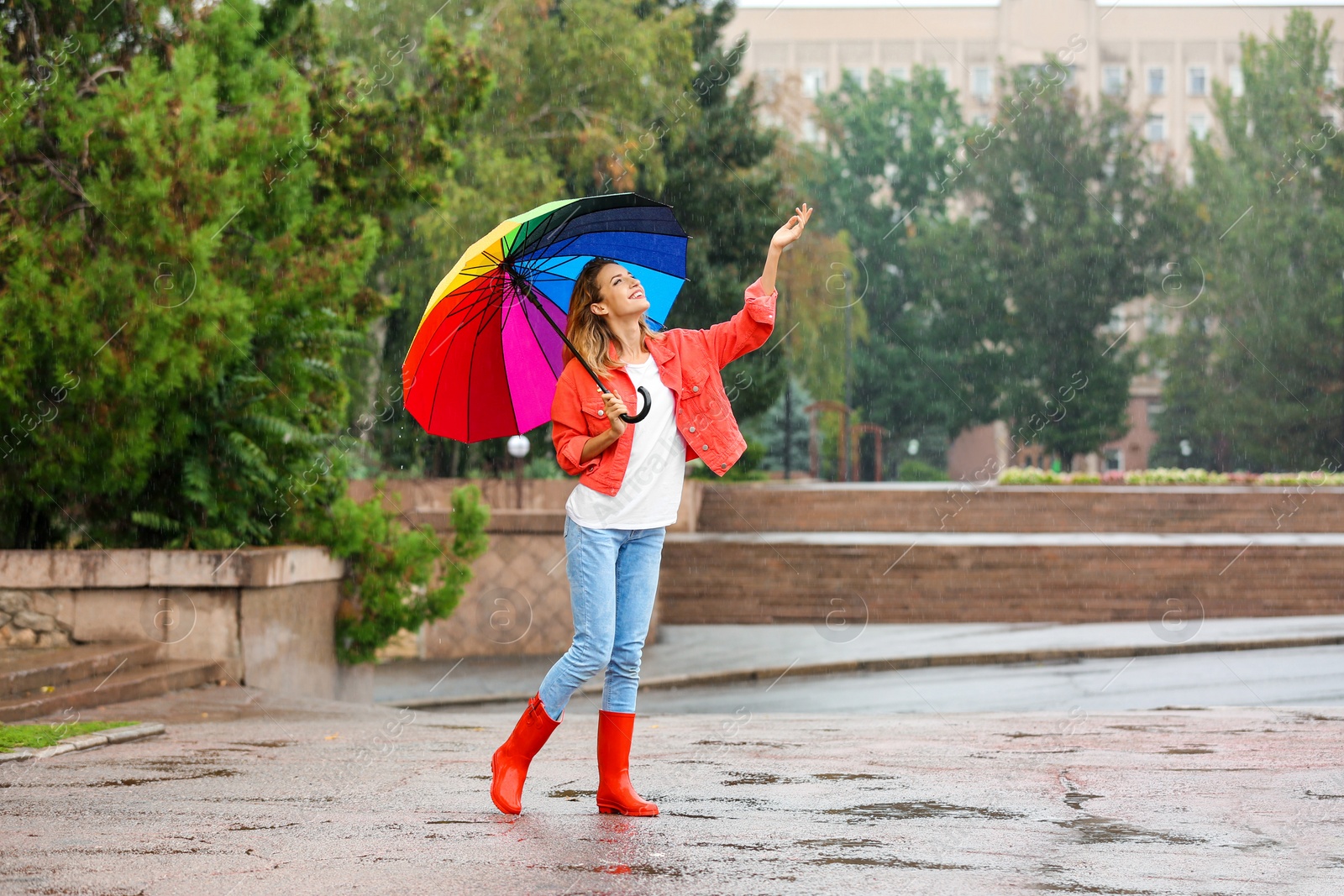 Photo of Happy young woman with bright umbrella under rain outdoors