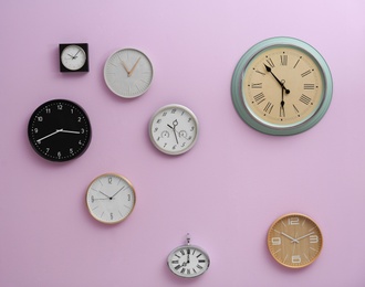 Photo of Many different clocks hanging on color wall. Time of day