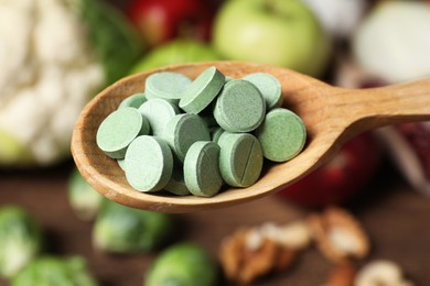 Photo of Wooden spoon of pills over table with foodstuff, closeup. Prebiotic supplements