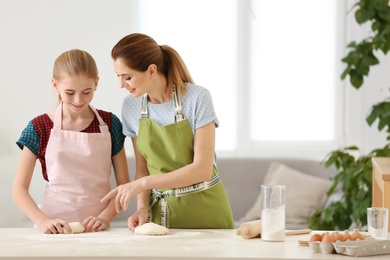 Photo of Mother and her daughter making dough at table in kitchen