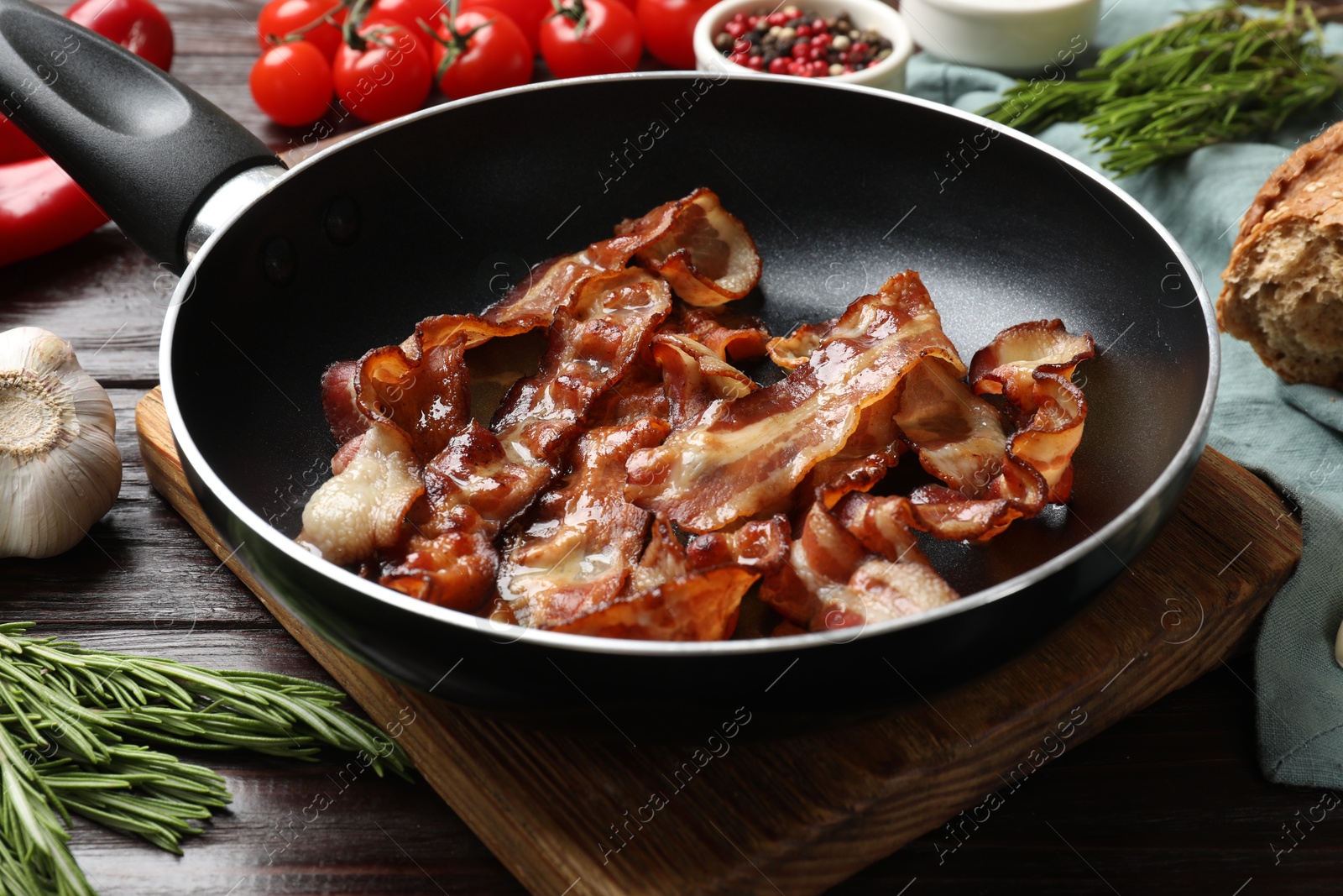 Photo of Delicious bacon slices in frying pan and products on wooden table, closeup