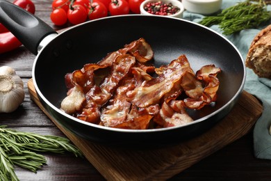 Photo of Delicious bacon slices in frying pan and products on wooden table, closeup