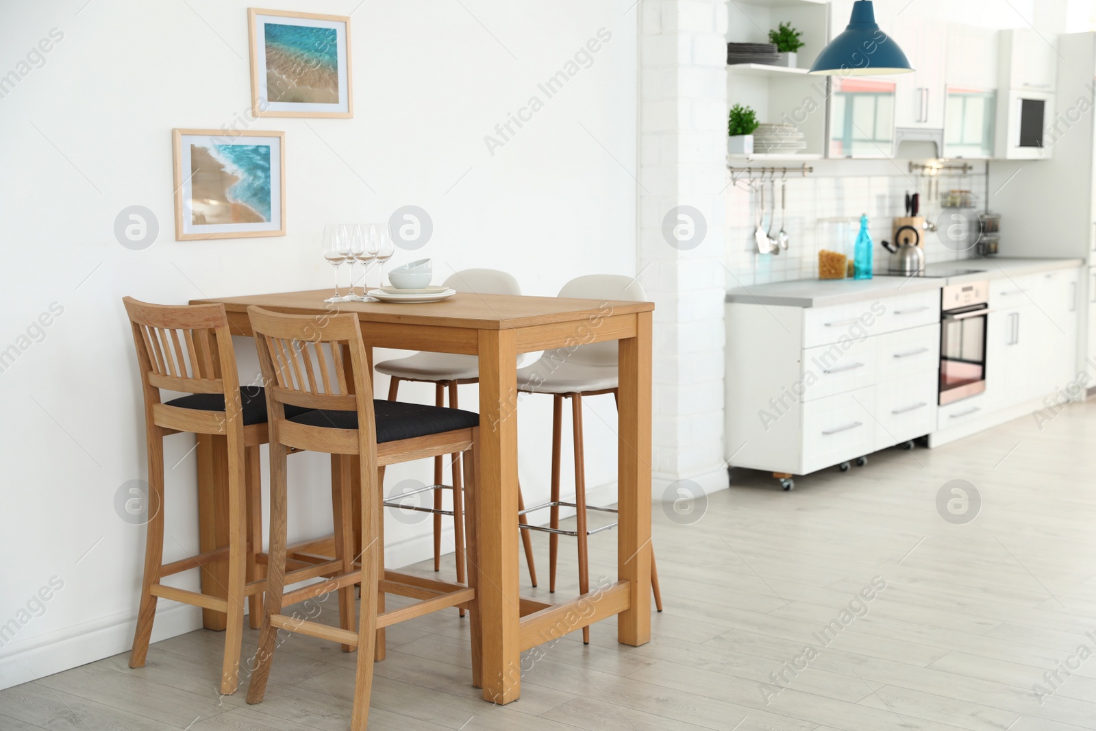 Photo of Stylish kitchen interior with dining table and bar stools near white wall