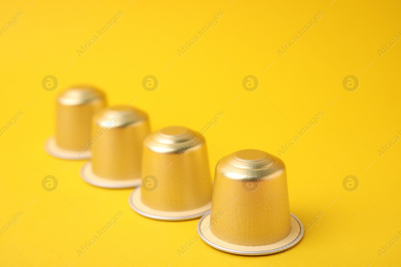 Photo of Many coffee capsules on yellow background, closeup