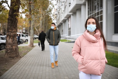 Photo of Young woman in medical face mask walking outdoors. Personal protection during COVID-19 pandemic