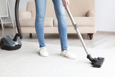 Photo of Woman cleaning carpet with vacuum in living room