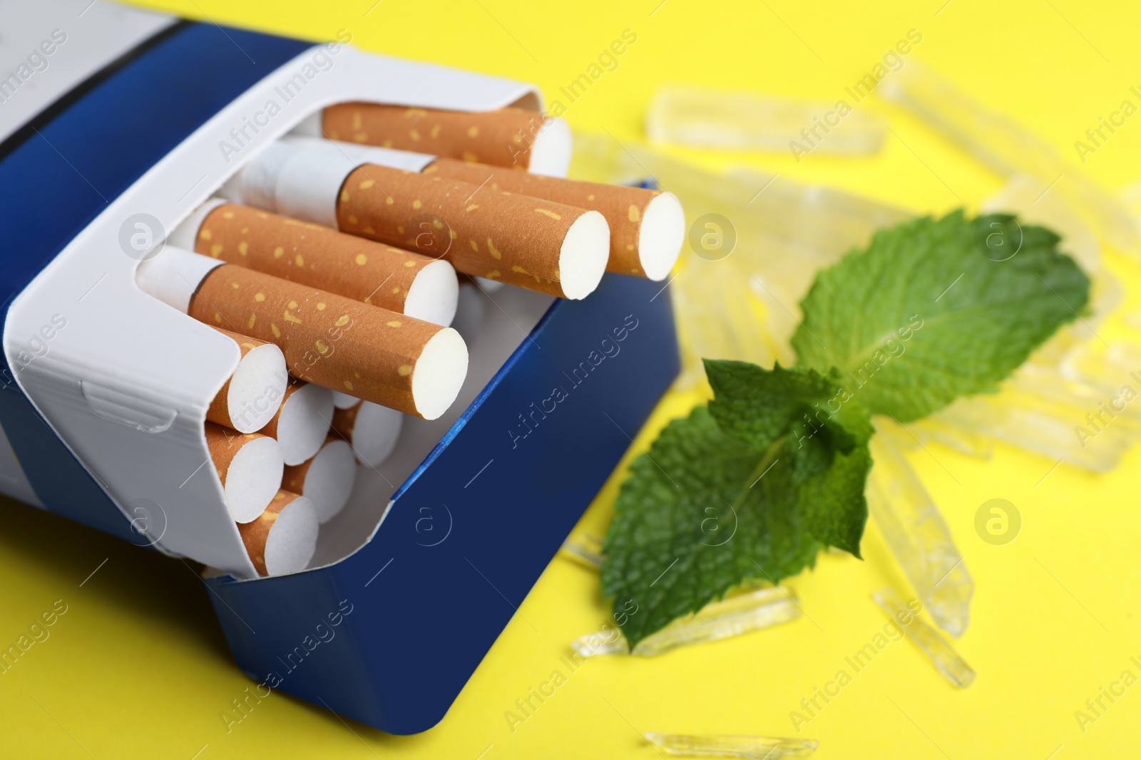 Photo of Pack of cigarettes, menthol crystals and mint on yellow background, closeup