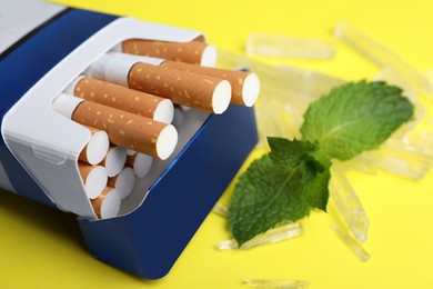 Photo of Pack of cigarettes, menthol crystals and mint on yellow background, closeup