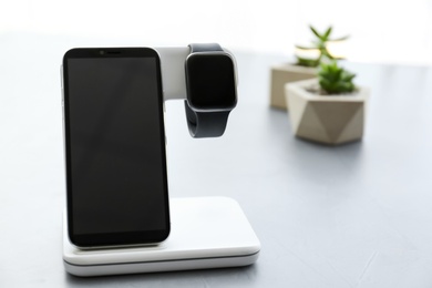 Photo of Stylish smart watch and phone charging with wireless pad on grey table