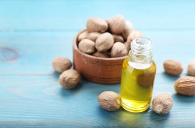 Photo of Bottle of nutmeg oil and nuts on turquoise wooden table, closeup. Space for text