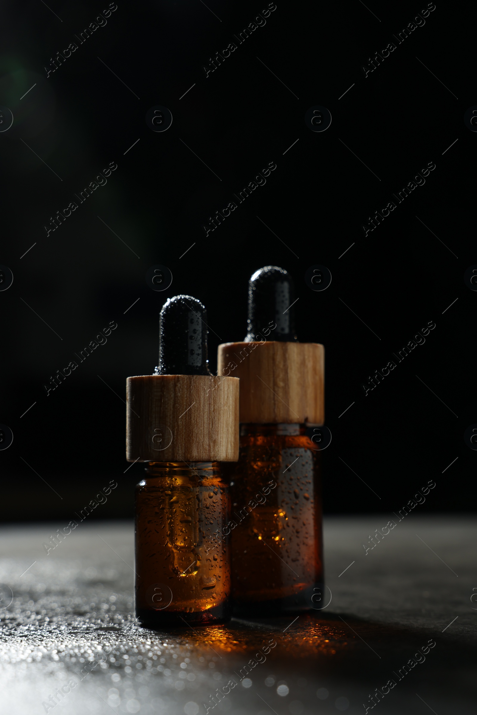 Photo of Bottles of cosmetic product on wet grey table against black background