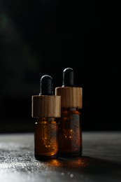 Photo of Bottles of cosmetic product on wet grey table against black background