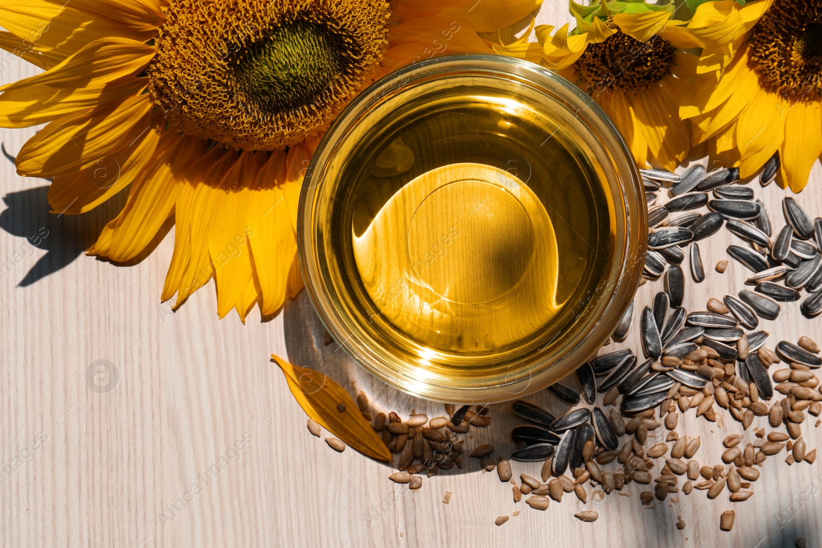 Photo of Sunflower oil in glass bowl and seeds on wooden table, flat lay