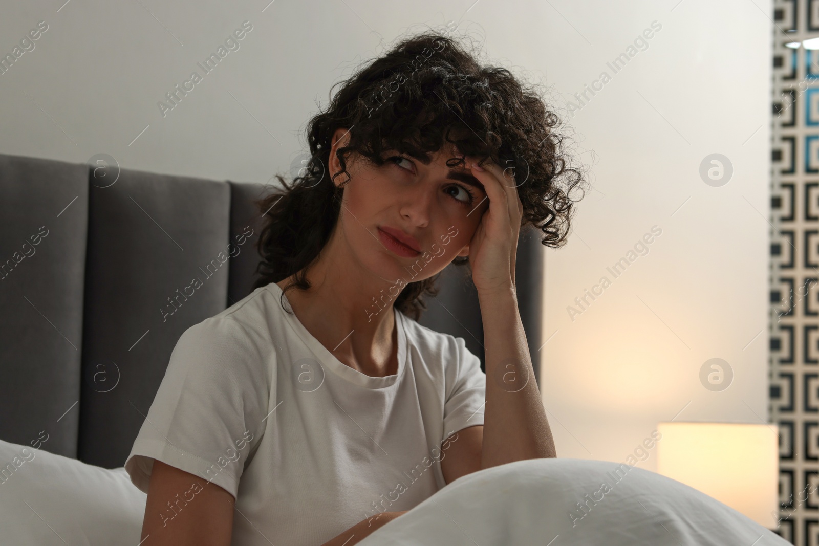 Photo of Young woman suffering from headache in bed at night