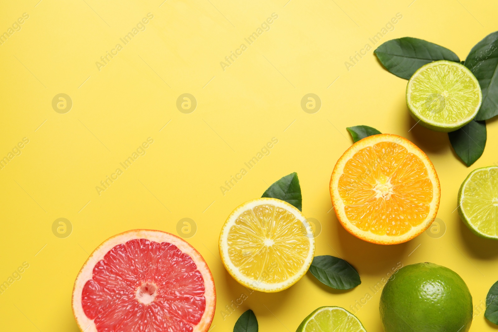 Photo of Different cut and whole citrus fruits on yellow table, flat lay. Space for text