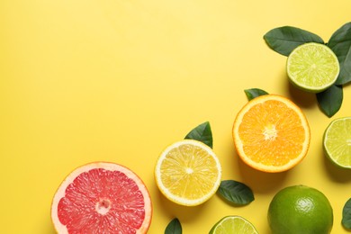 Photo of Different cut and whole citrus fruits on yellow table, flat lay. Space for text