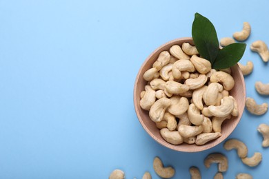 Photo of Many tasty cashew nuts and leaves on light blue background, top view. Space for text