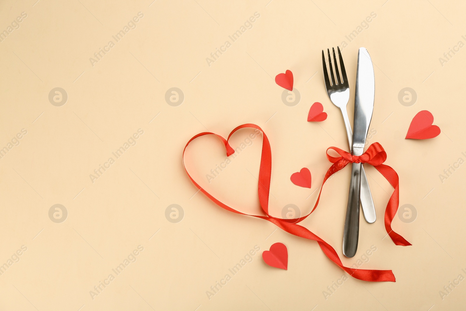 Photo of Beautiful cutlery set, hearts and red ribbon on beige background, flat lay with space for text. Valentine's Day dinner