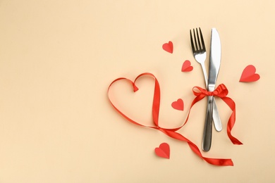 Beautiful cutlery set, hearts and red ribbon on beige background, flat lay with space for text. Valentine's Day dinner