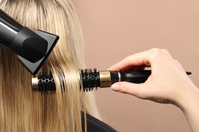 Hairdresser blow drying client's hair on beige background, closeup