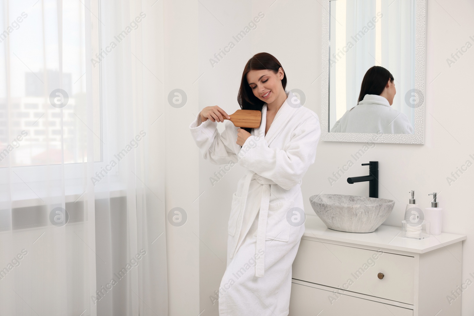 Photo of Beautiful woman brushing her hair in bathroom, space for text