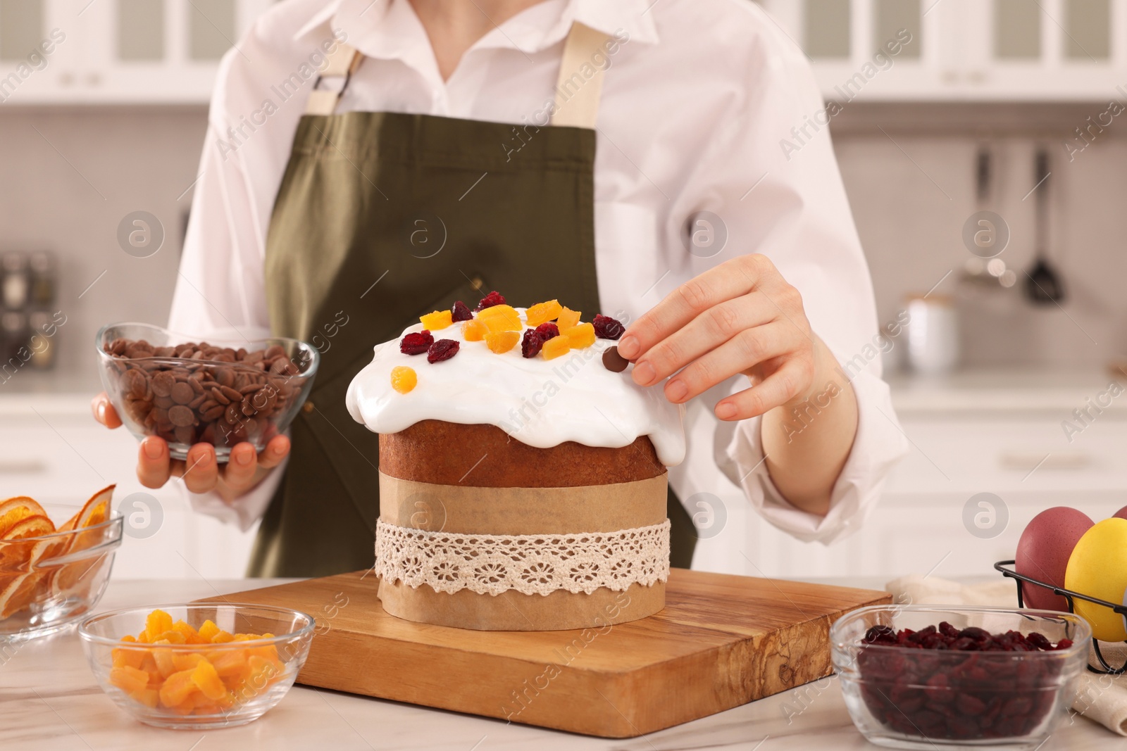 Photo of Woman decorating delicious Easter cake with chocolate pieces at white marble table in kitchen, closeup