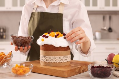 Woman decorating delicious Easter cake with chocolate pieces at white marble table in kitchen, closeup