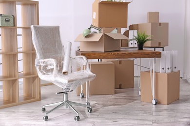 Photo of Armchair and carton boxes with stuff in room. Office move concept