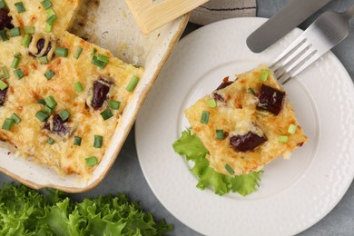 Photo of Tasty sausage casserole with green onions served on grey table, flat lay