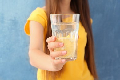 Young woman holding glass of lemon water on color background, closeup