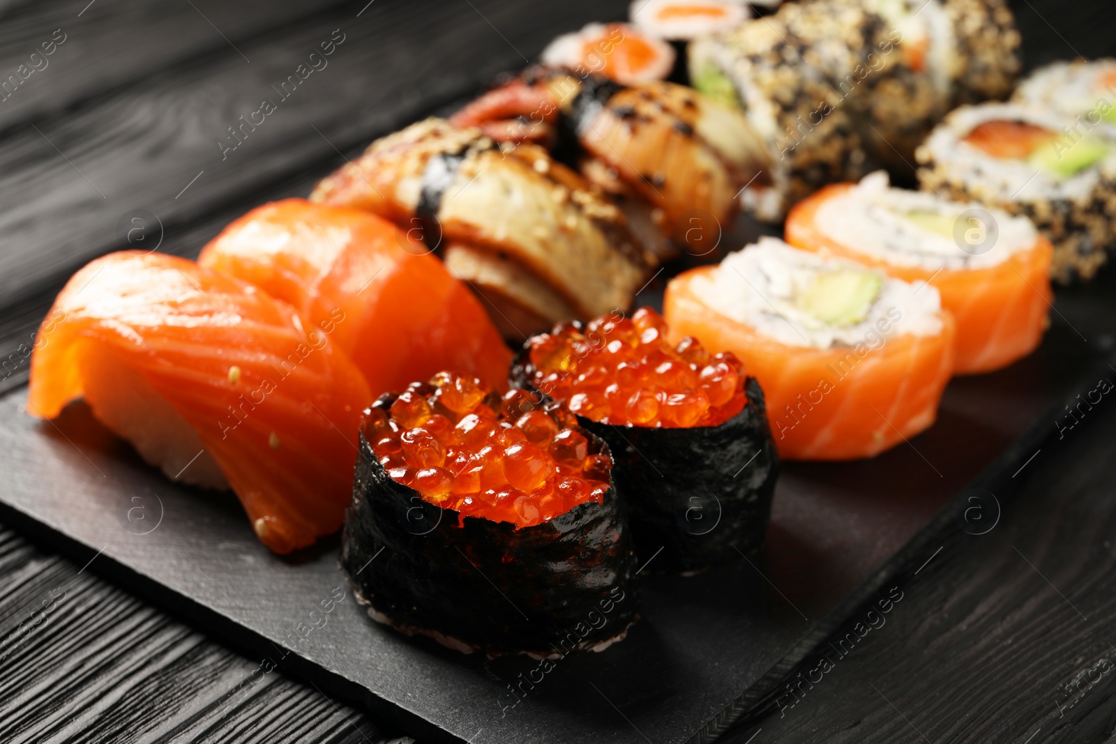 Photo of Set of delicious sushi rolls on black wooden table, closeup