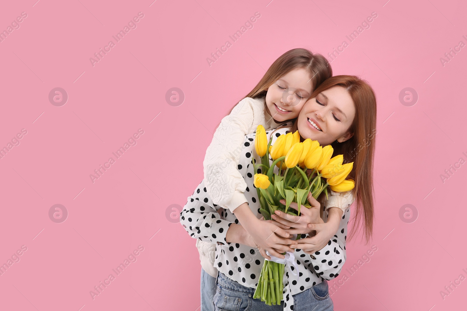Photo of Mother and her cute daughter with bouquet of yellow tulips on pink background. Space for text