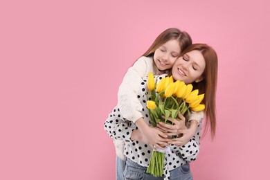 Photo of Mother and her cute daughter with bouquet of yellow tulips on pink background. Space for text