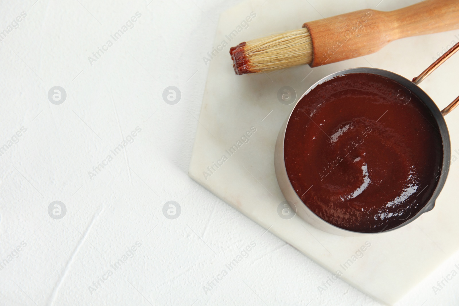 Photo of Cooking pot with barbecue sauce and brush on white background, flat lay. Space for text