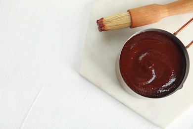 Photo of Cooking pot with barbecue sauce and brush on white background, flat lay. Space for text