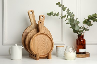 Photo of Wooden cutting boards, teapot, candle and vase with eucalyptus branches on white table