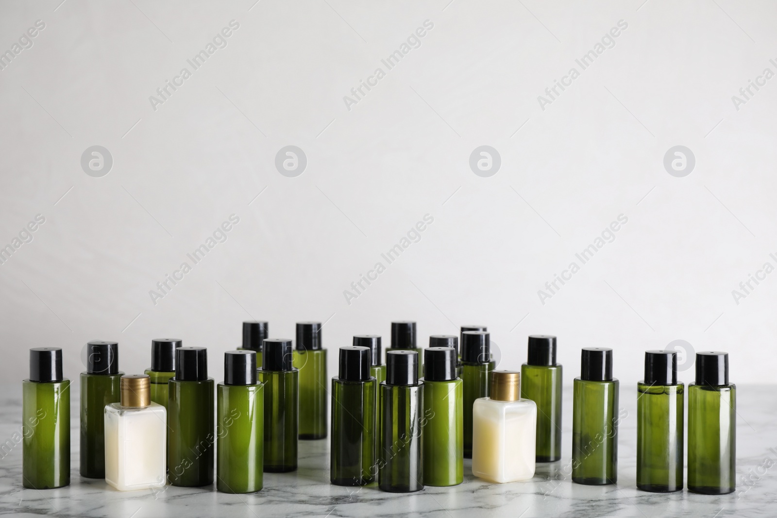 Photo of Mini bottles with cosmetic products on white marble table against light background