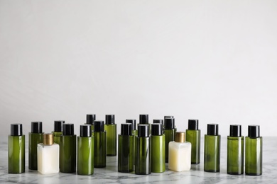 Mini bottles with cosmetic products on white marble table against light background