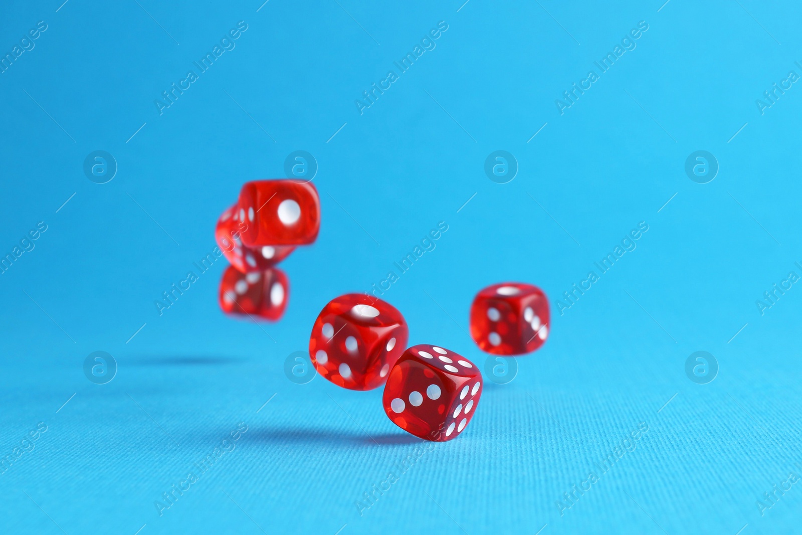 Photo of Many red game dices falling on light blue background. Space for text