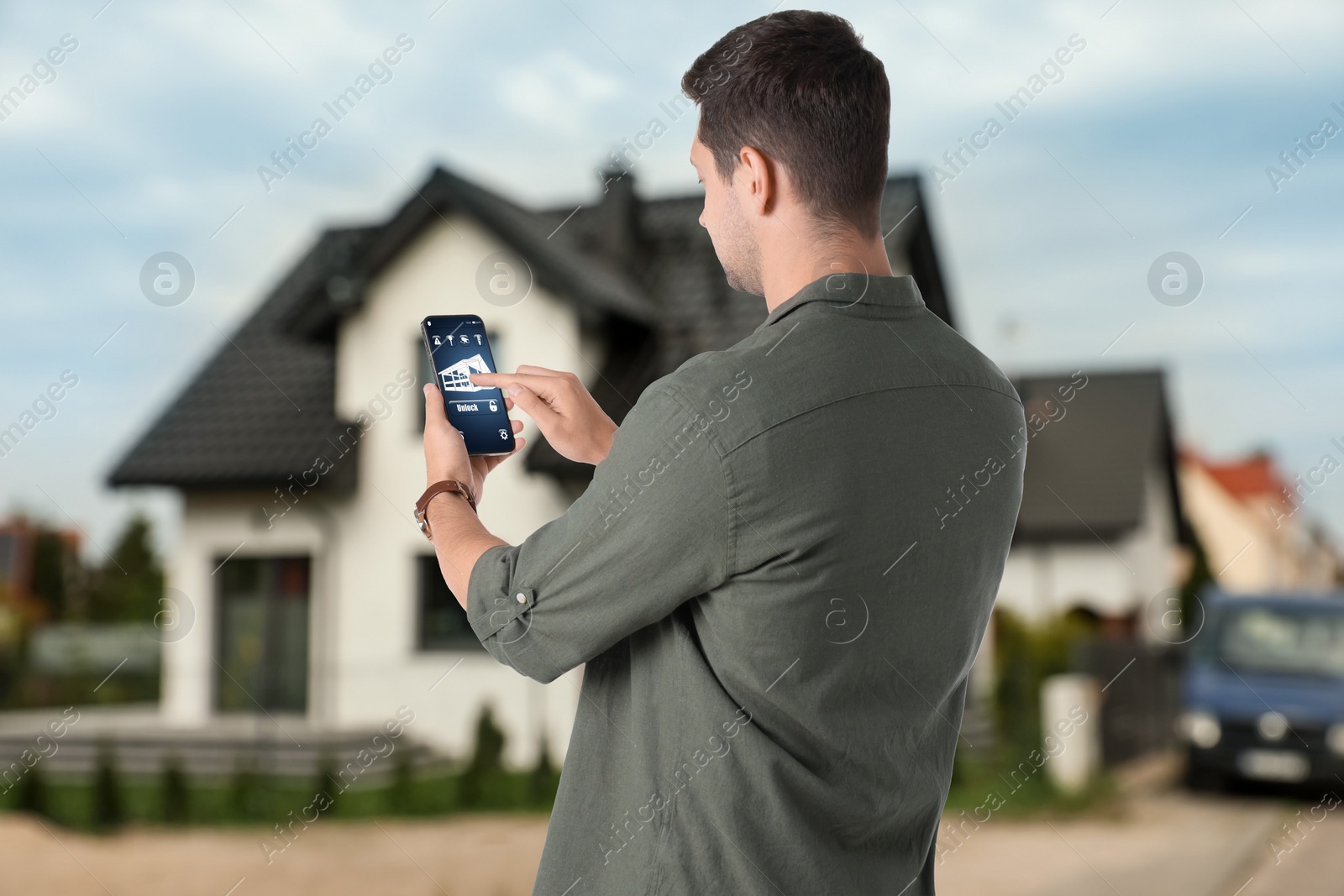 Image of Man using home security system application on smartphone outdoors
