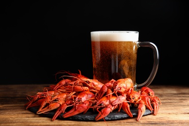 Photo of Delicious red boiled crayfishes and mug of beer on wooden table
