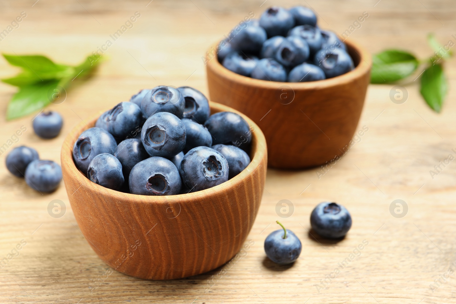 Photo of Bowls of fresh tasty blueberries on wooden table, closeup
