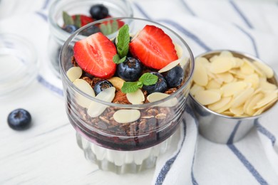 Photo of Tasty granola with berries, jam, yogurt and almond flakes in glass on white table, closeup