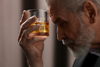 Photo of Senior man holding glass of whiskey with ice cubes on brown background, closeup