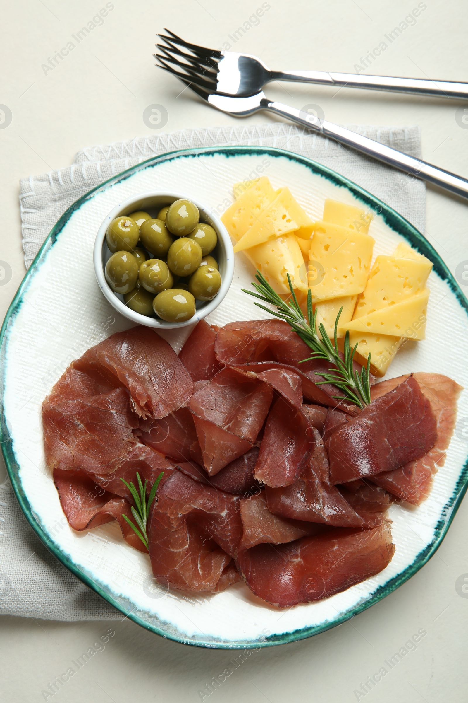 Photo of Delicious bresaola, cheese, olives and rosemary served on light textured table, top view